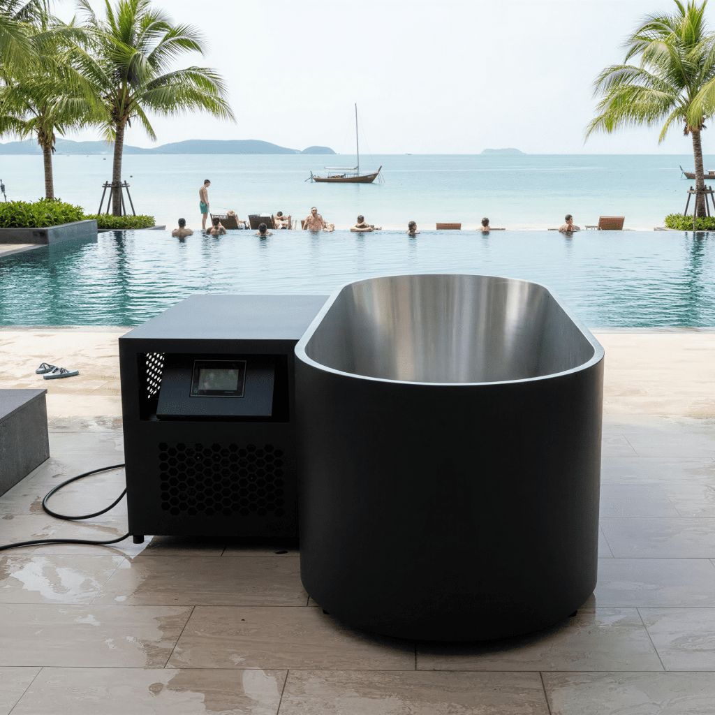 Black steel ice bath with chiller beside a beachfront pool, islands in the background