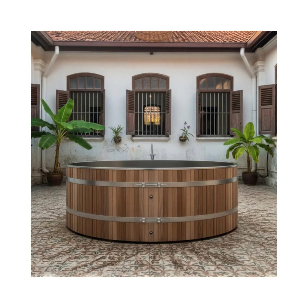 Circular outdoor cold plunge tub with vertical timber slat exterior, stainless steel interior and banding, positioned in a tiled courtyard setting.