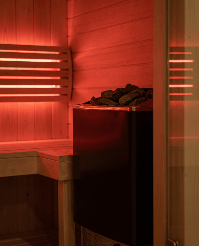Sauna interior in warm red light showing the stone heater and timber wall slats