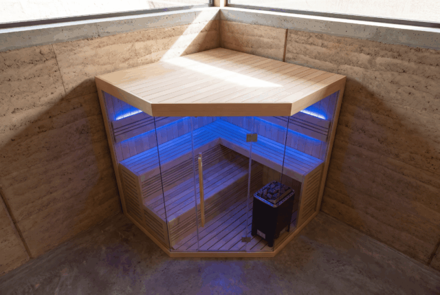 Corner sauna with glass front lit blue, set into a stone-walled room, seen from above